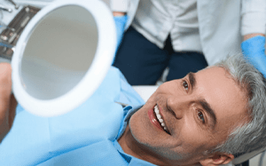 a man smiling while looking in a handheld mirror